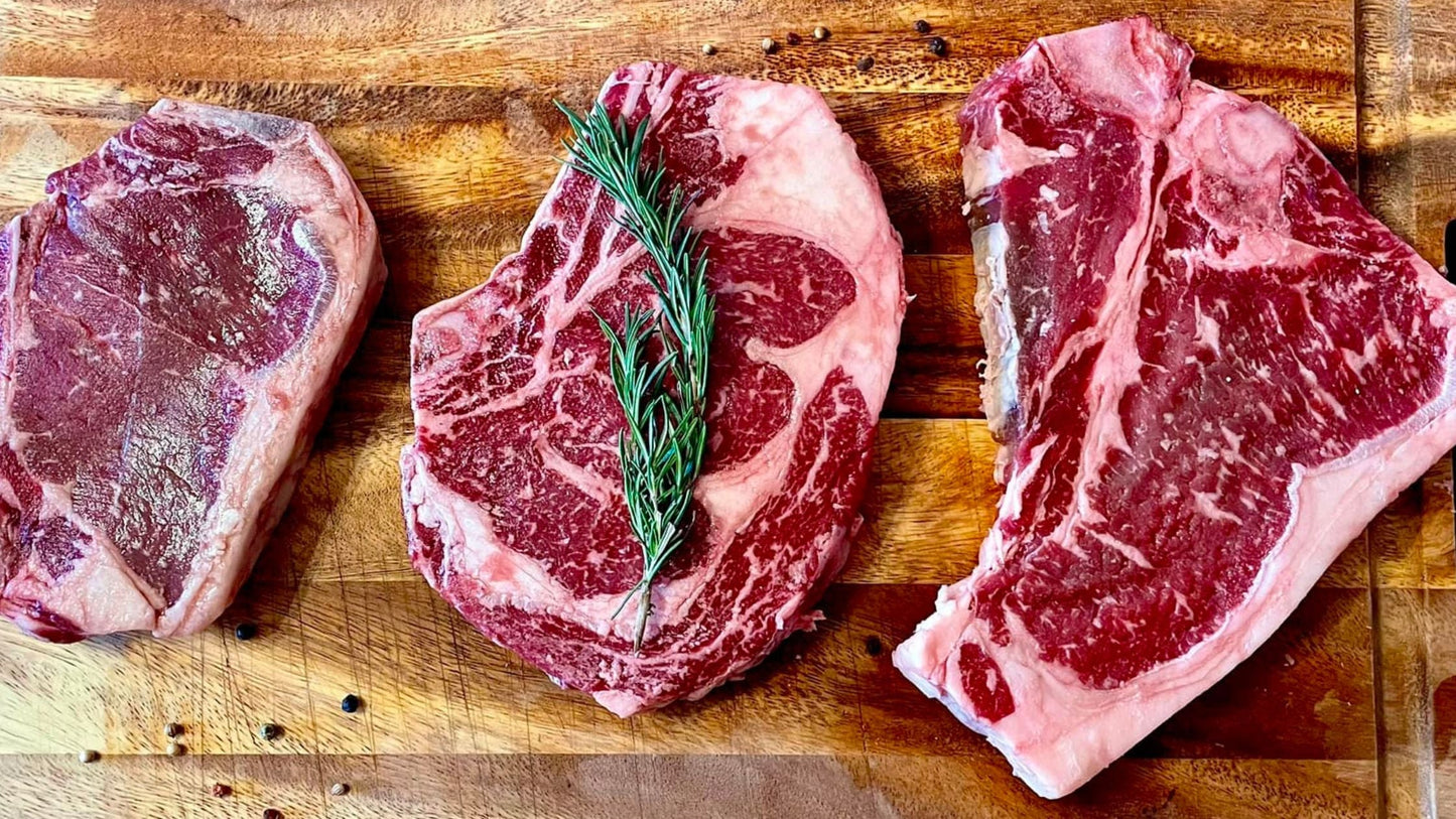 Three cuts of premium dry-aged angus beef from KL Beef Co. displayed on a wooden board, highlighting marbling and quality of Nebraska-raised angus meat.