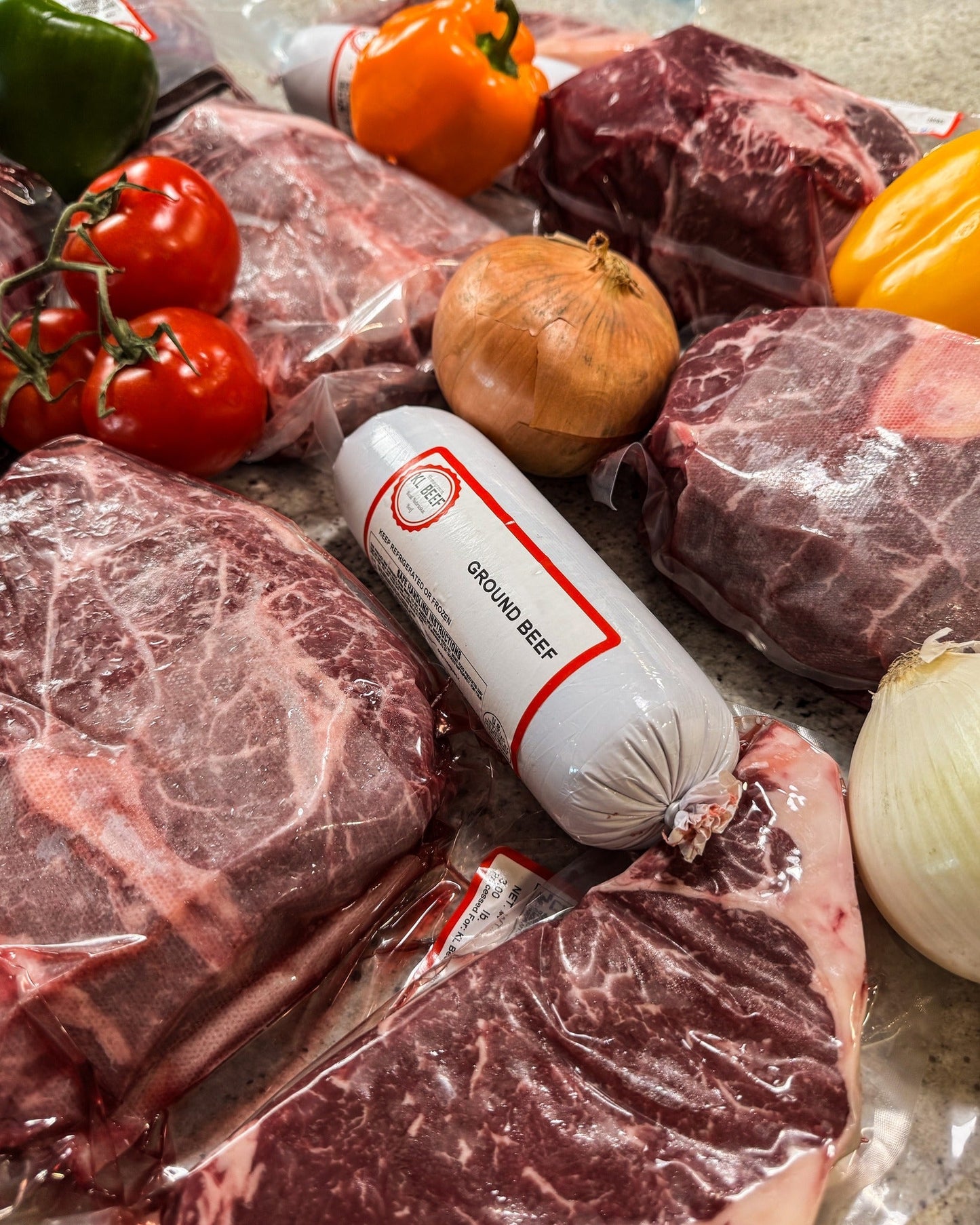 Vacuum-sealed cuts of Nebraska bulk beef for sale from KL Beef Co., including steaks and ground beef, displayed with fresh vegetables.