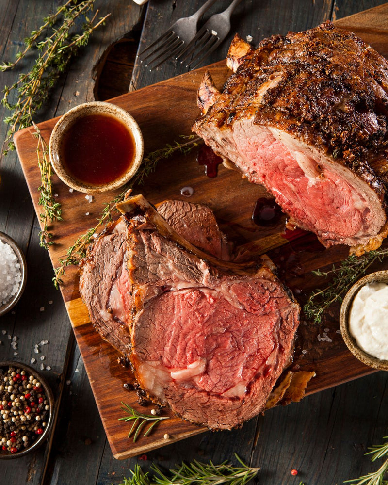 Sliced prime rib roast made from dry-aged Nebraska beef, served on a rustic cutting board with au jus, herbs, and seasoning.